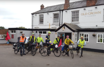 Image of a group of cyclists in front of a pub in high-visibility clothing, photographer unknown