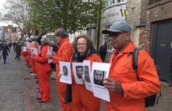 Lewes Amnesty Group in a line wearing orange jumpsuits, holding up photos of the 39 men still detained at Guantanamo Bay