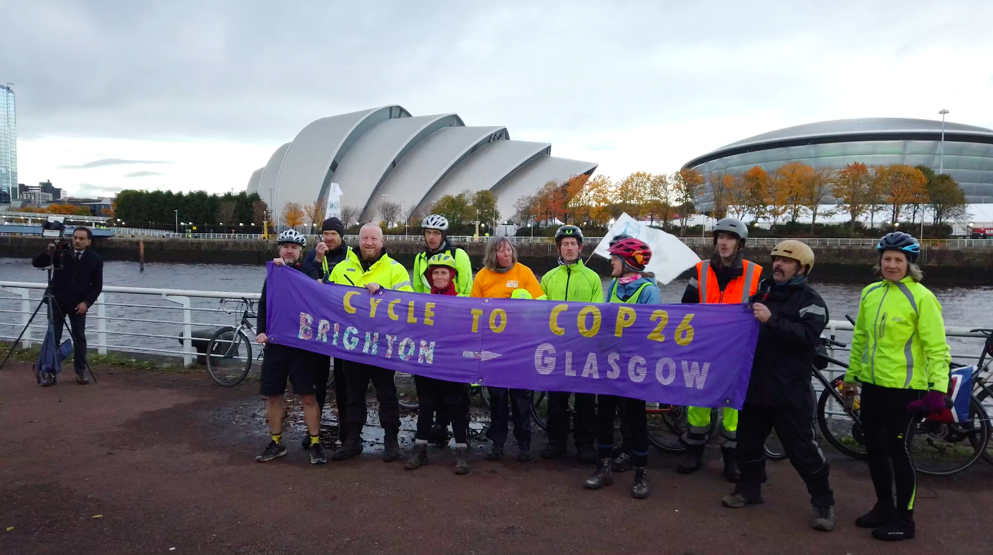 Members of the Brighton to Glasgow Bike ride pose with a banner at the end of their journey